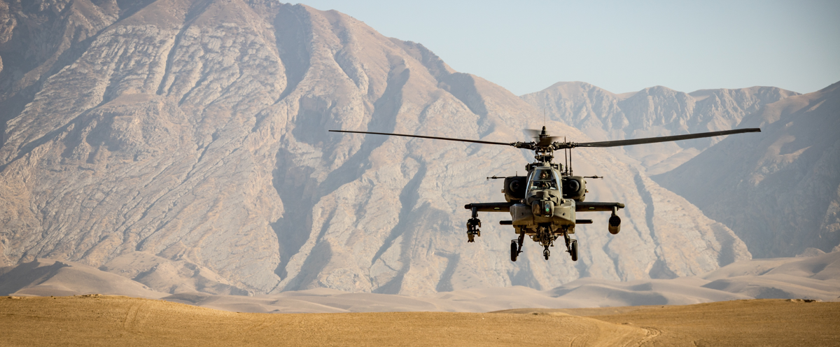 A helicopter flying over a desert landscape with mountains in the background.