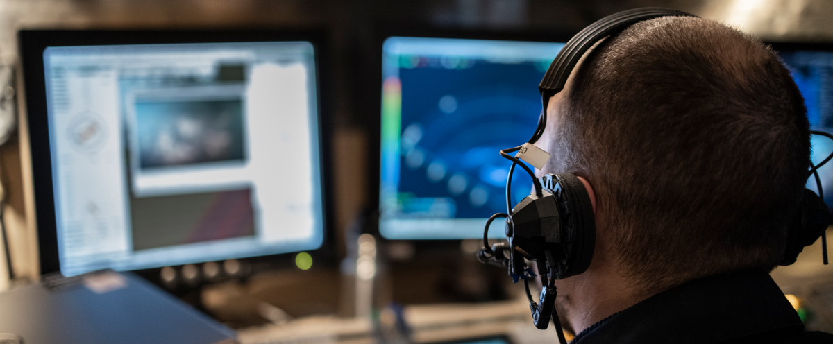 A man wearing headphones sitting in front of two monitors.