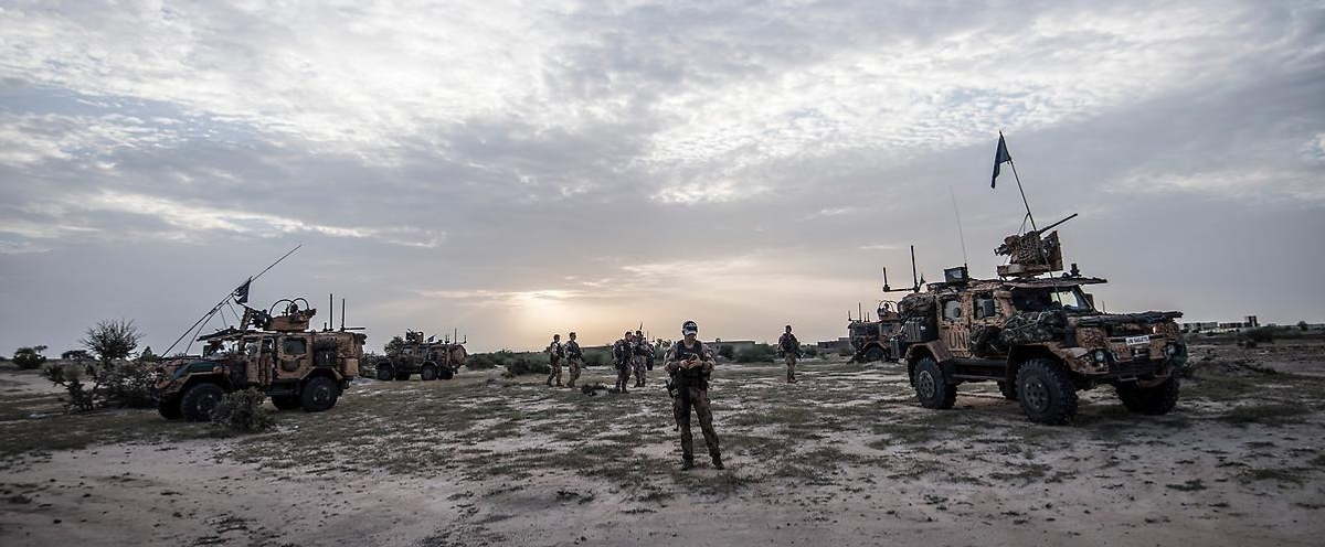 A group of military vehicles parked on top of a dirt field.