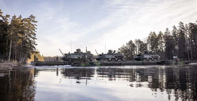 Militära fordon transporteras över vattendrag.