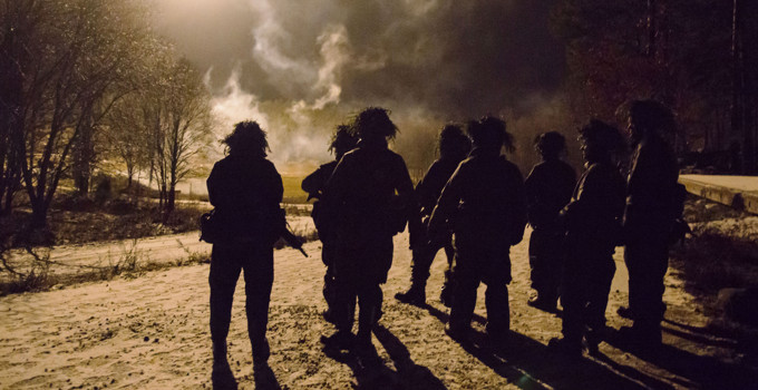 En grupp militärer på övning står på snötäckt grusväg på natten.