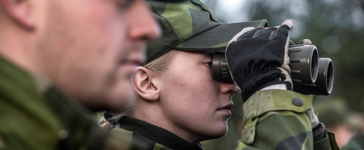 A man and a woman in camouflage looking through binoculars.