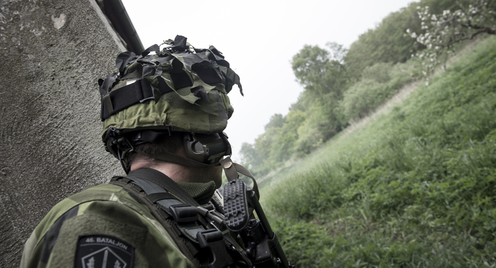 Soldat med kamouflagekläder bakifrån som tittar mot ett grönområde.