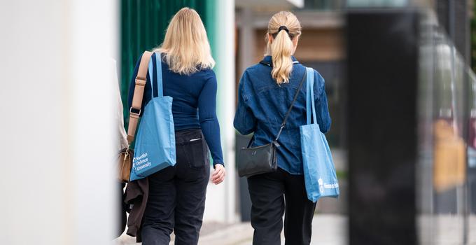 Två kvinnor med ryggen mot kameran som går utomhus. 